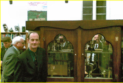 Former Maths teacher Des Williams in front of the John Arbery Memorial Cabinet in the Resource Centre